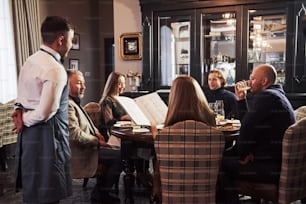 Waiter is waiting for an order. Family friends having nice time in beautiful luxury modern restaurant.