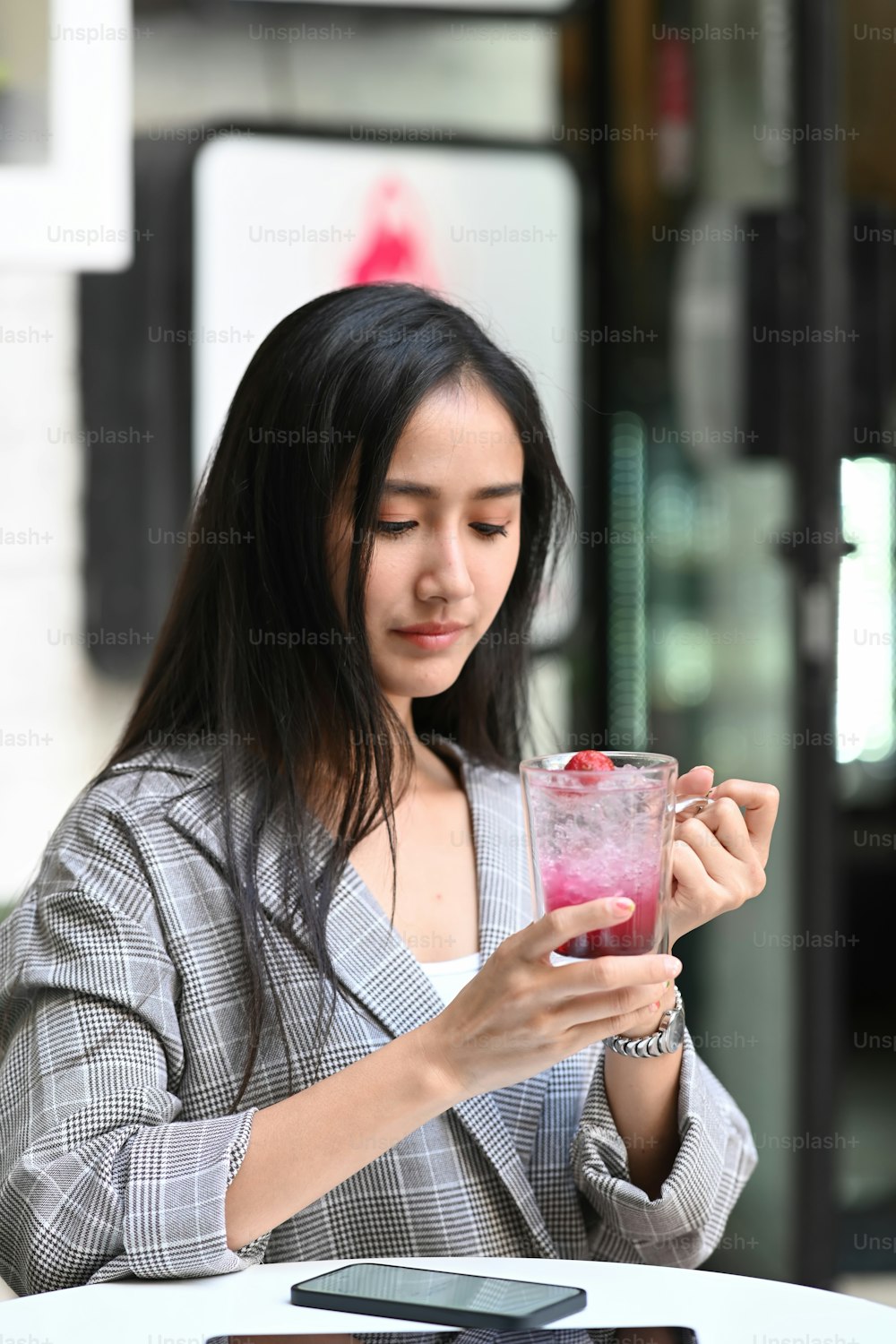 Portrait of young woman holding glass of raspberry refreshing drink while sitting at cafe.
