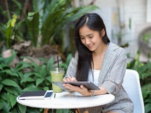 Retrato de mujer de negocios que trabaja con tableta digital en mesa de café en el jardín de la casa