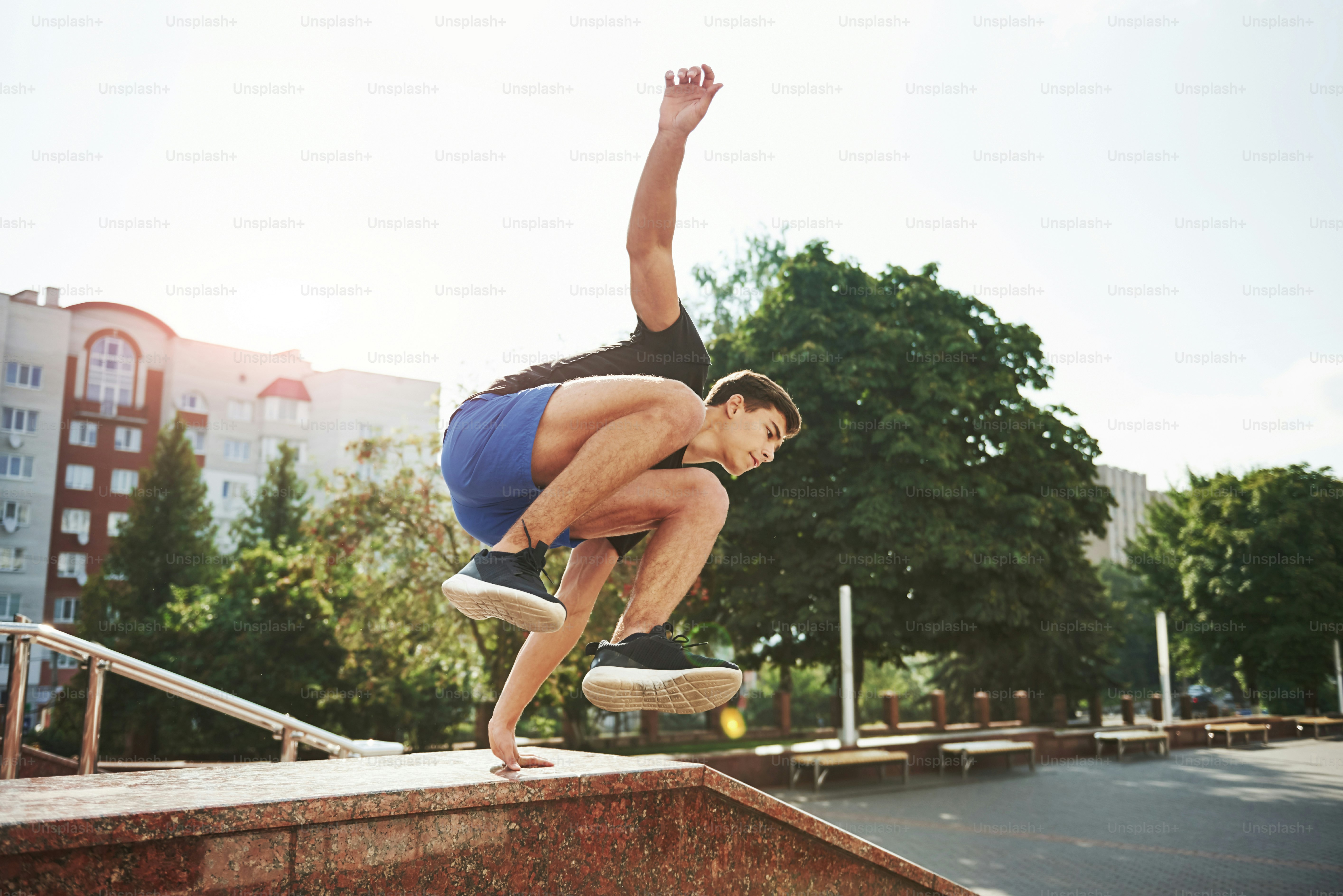 Natural lighting. Young sports man doing parkour in the city at sunny daytime.