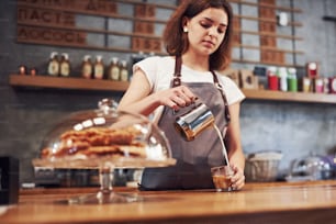 Pouring fresh coffee. Young female worker indoors. Conception of business and service.