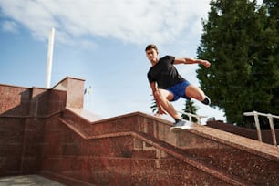 Above the obstacle. Young sports man doing parkour in the city at sunny daytime.