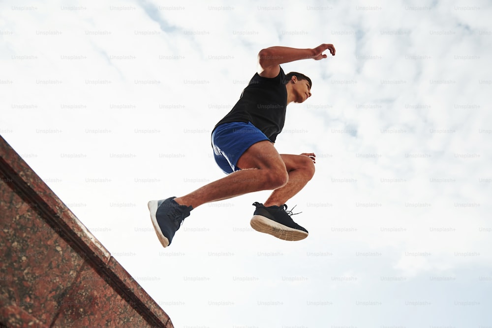 Cloudly sky. In the air. Young sports man doing parkour in the city at sunny daytime.