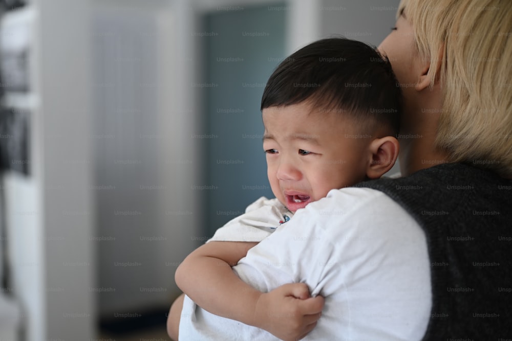 Une mère essaie de calmer son petit garçon qui pleure tout en se tenant dans une maison confortable.