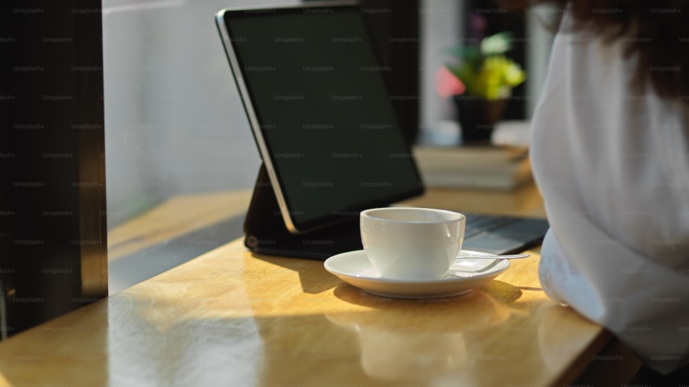Close up view of coffee cup and digital table on wooden bar with female customer in cafe