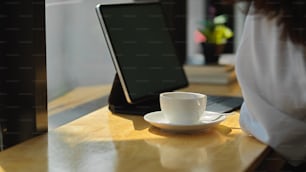 Vista de cerca de la taza de café y la mesa digital en la barra de madera con una clienta en la cafetería