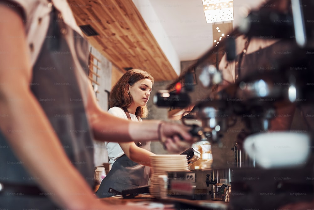 Prozess der Herstellung von frischem Getränk. Mit Maschine. Zwei junge Café-Arbeiter drinnen. Konzeption von Geschäft und Service.