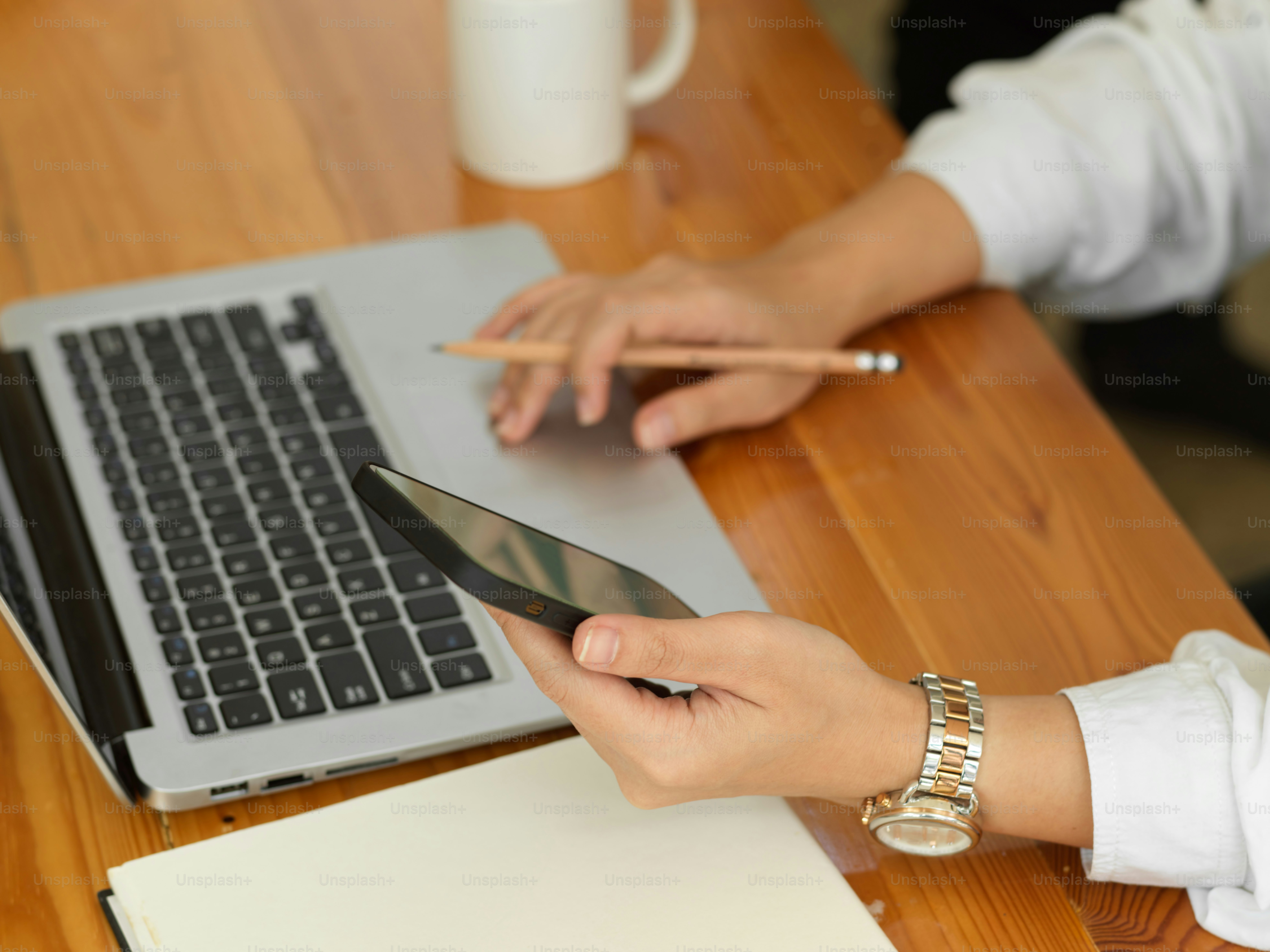 Cropped shot of female hand working with smartphone, laptop and stationery on wooden table