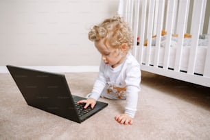 Cute blonde curly toddler baby boy working on laptop. Little kid child using technology. Early age education development. Video chat, video call. Computer screen time for children.