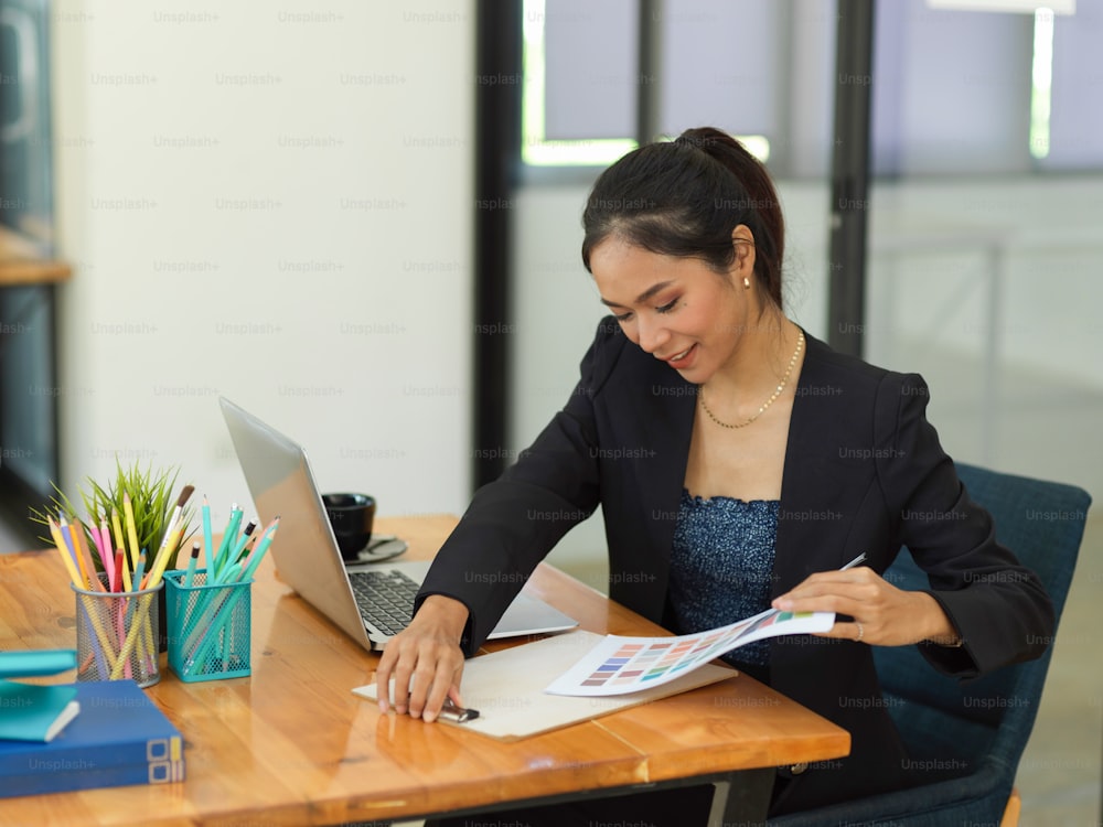 Porträt einer Geschäftsfrau, die mit Papierkram auf einem Holztisch mit Büromaterial im Büroraum arbeitet