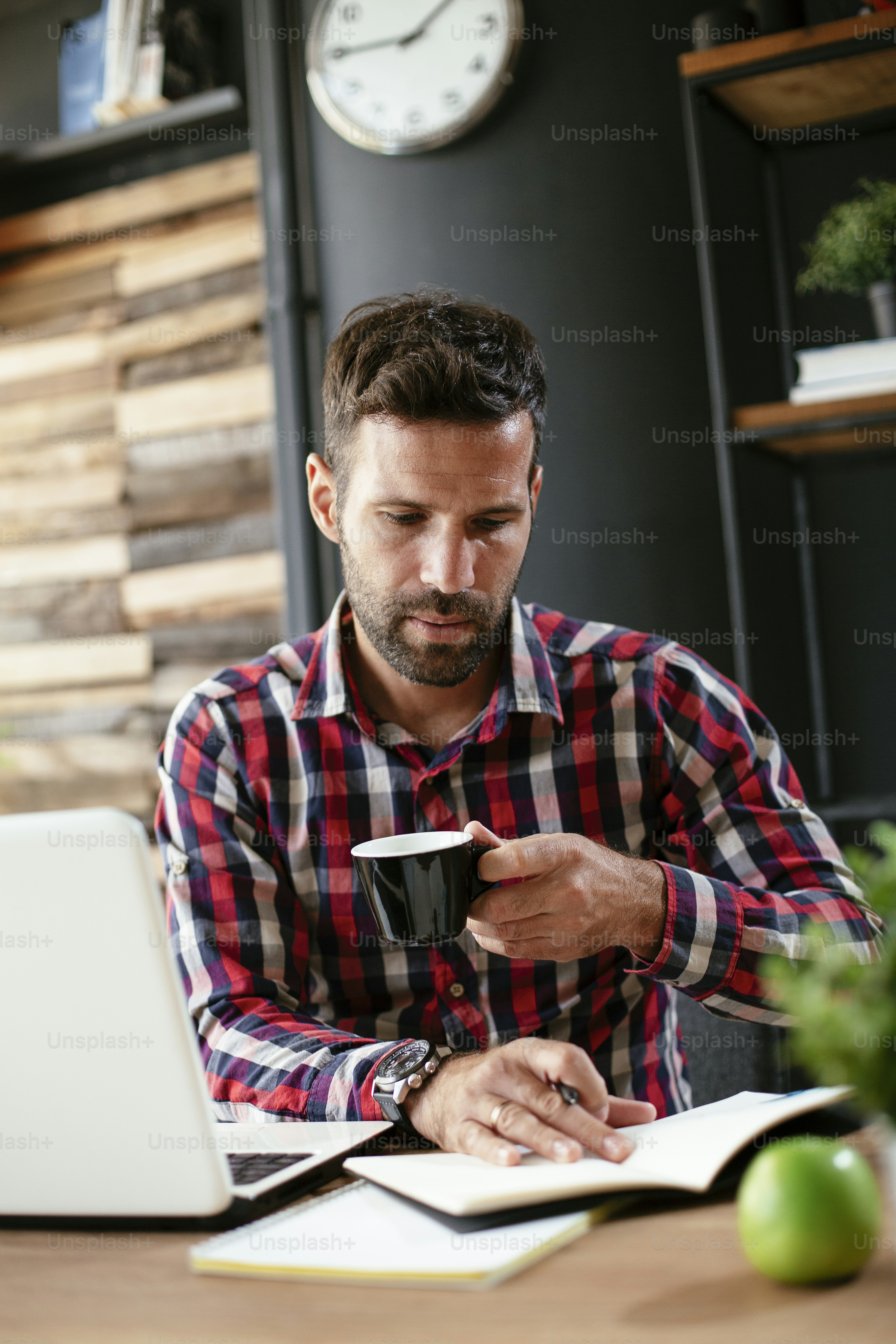 Young businessman using laptop and drinking coffee in his office. Handsome man on coffee break.