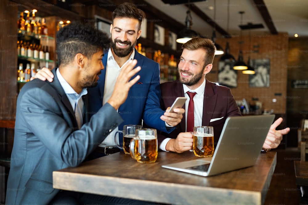 Happy young businessmen in suits are smiling and talking in a pub