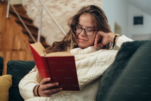 Shot of a young woman reading a book while sitting on the couch at home
