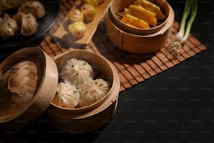 Colpo ritagliato di piroscafi di bambù con gnocchi e panino di maiale sul tavolo da pranzo in un ristorante cinese