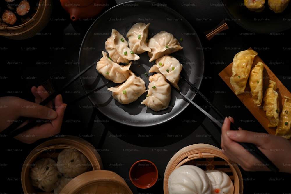 Vue de dessus de la table à manger dans un restaurant chinois, les mains des gens avec des baguettes cueillant des boulettes de Dimsum