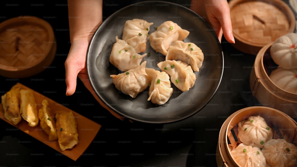 Vista superior das mãos femininas segurando um prato de bolinhos de massa para servir na mesa Dimsum no restaurante chinês