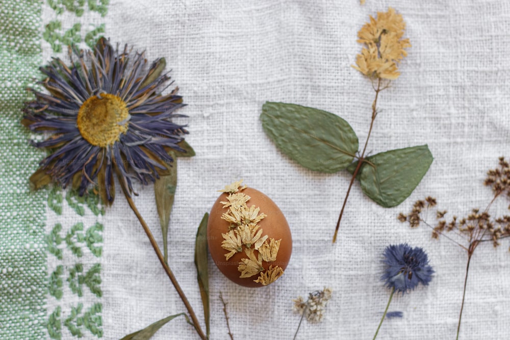 Huevo de Pascua decorado con flor seca sobre fondo de servilleta de lino y flores silvestres. Vista superior. Decoración ecológica natural creativa de huevos de pascua