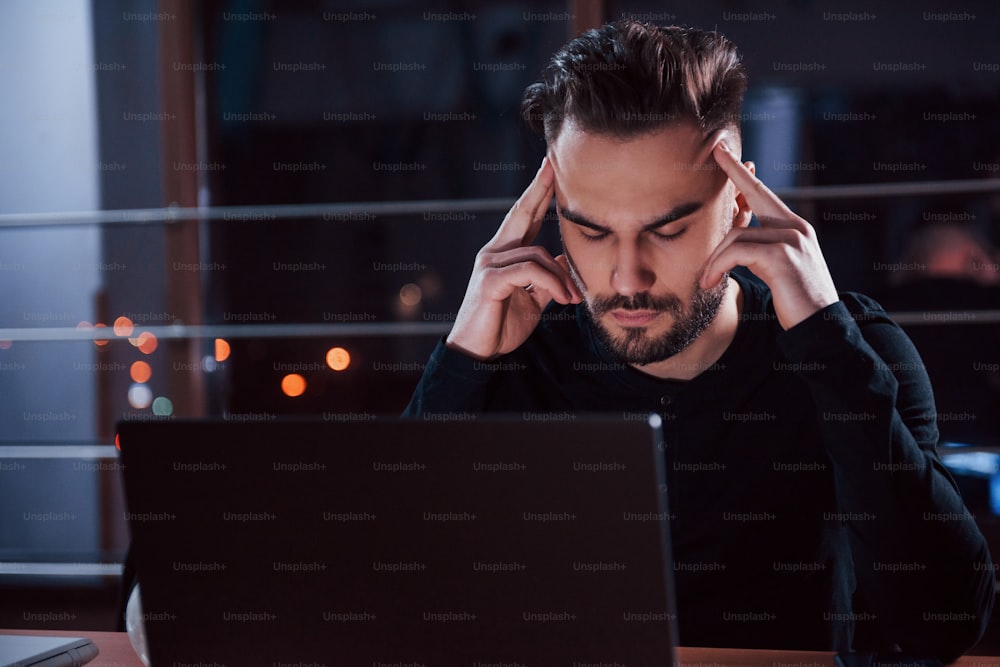 Stressful situation. Stylish young businessman works alone in the office at nightime.