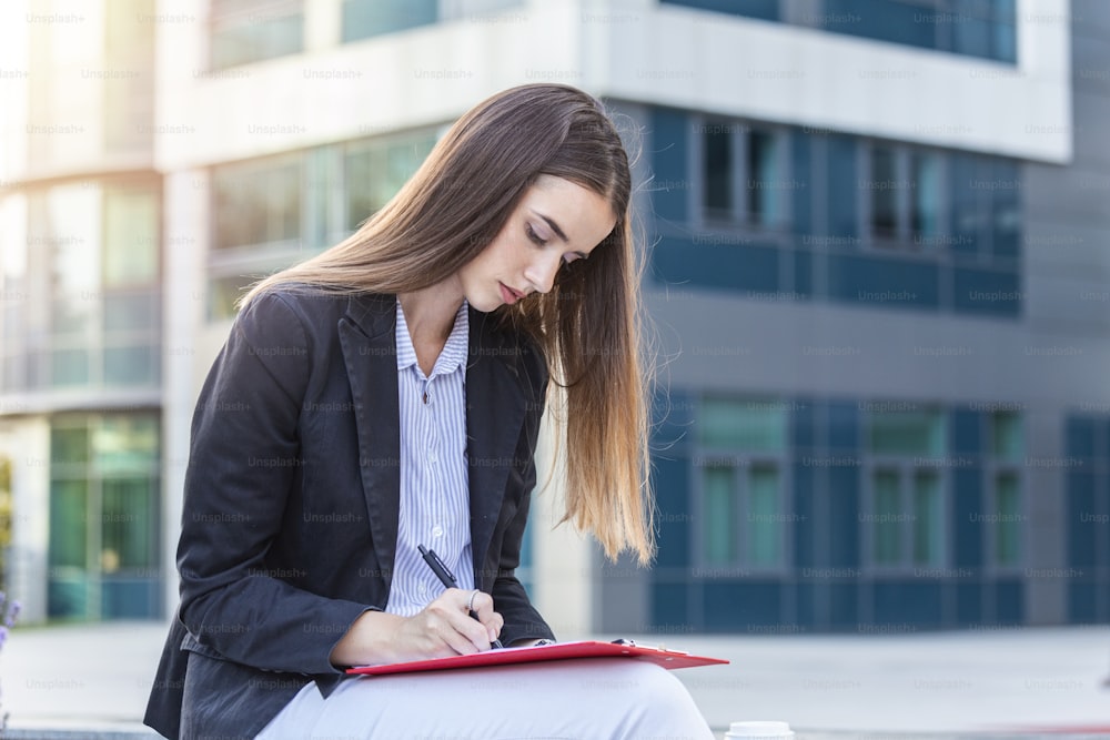 Executive business woman with clipboard against the urban background, Portrait of confident business woman with clipboard making notes