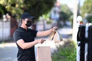 L'uomo asiatico di consegna indossa una maschera protettiva e consegna cibo alla porta.