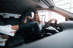 Cheerful mood. Girl in modern car in the salon. At daytime indoors. Buying new vehicle.