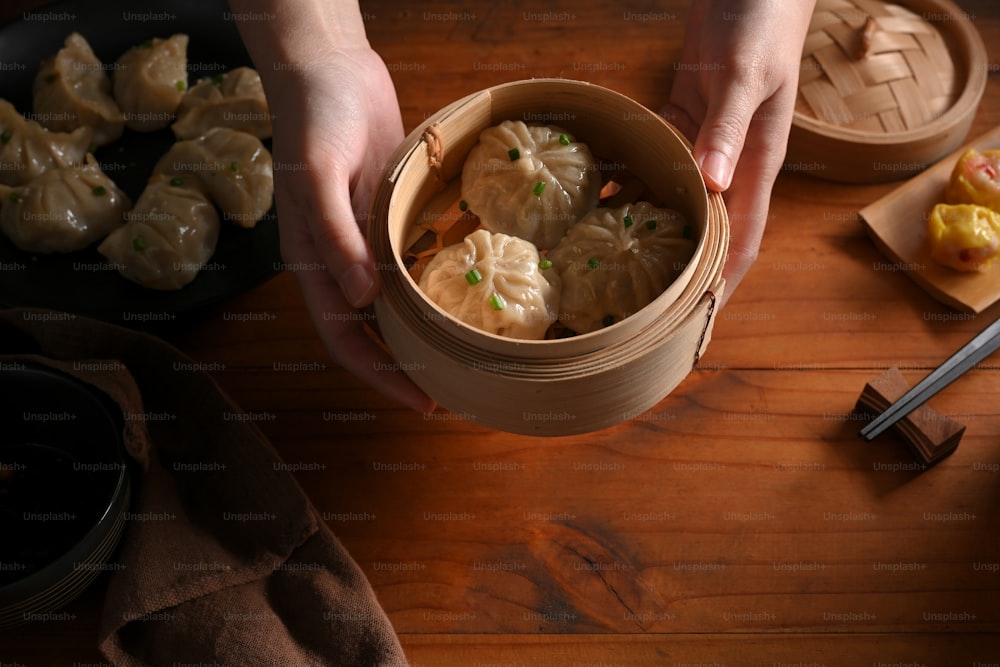 Top view of female hands holding a bamboo steamer of Dimsum dumplings to serve in restaurant