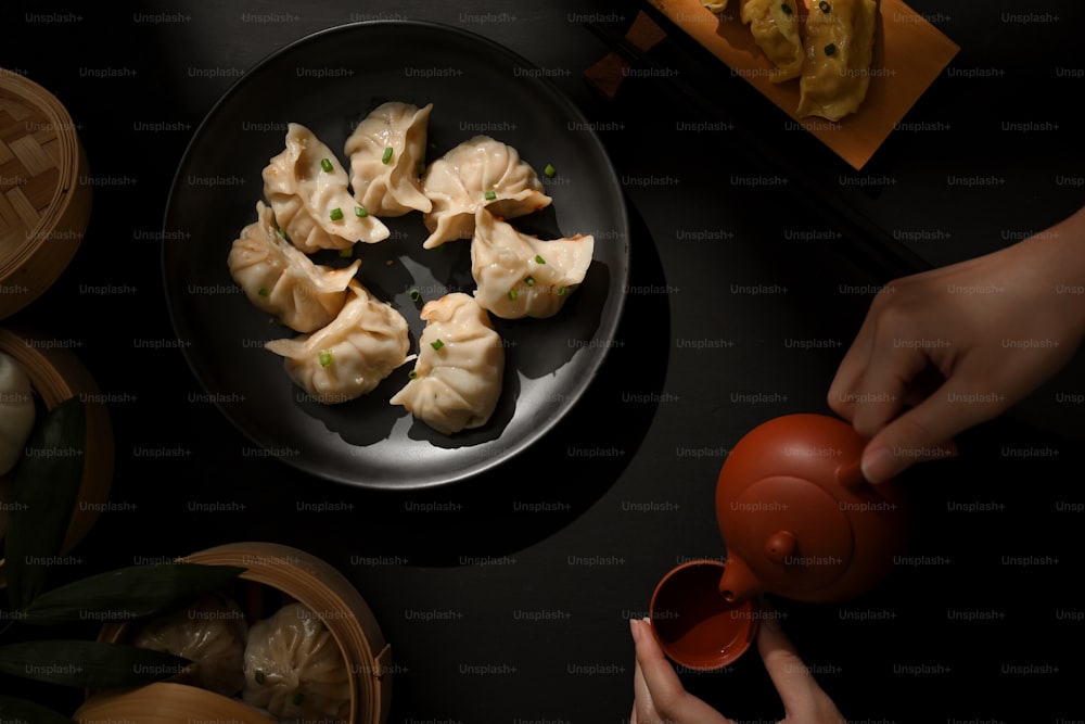 Vista superior de la mesa de comedor con albóndigas de dimsum y mano femenina con tetera en restaurante chino