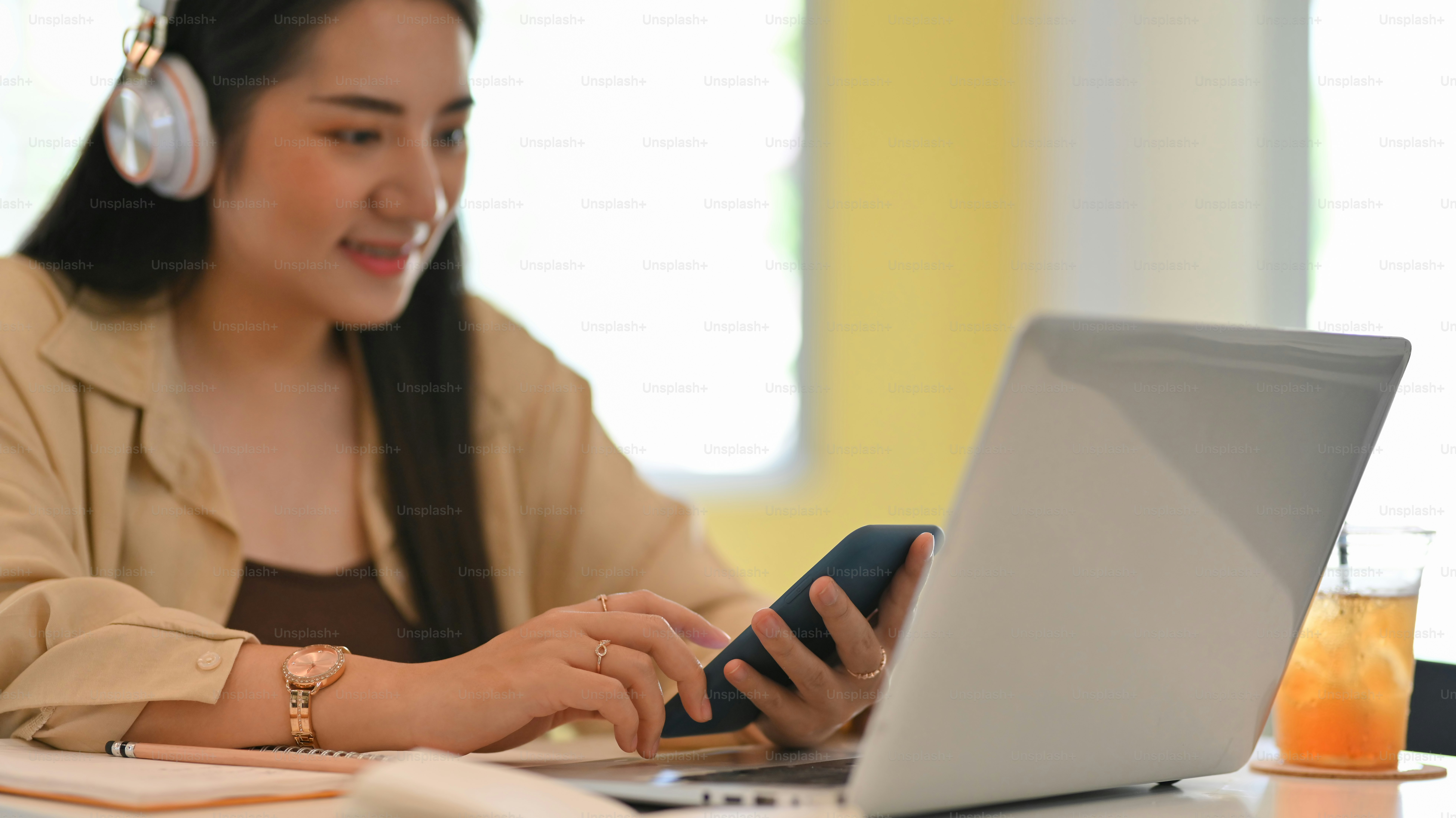 Tampilan dekat remaja perempuan dengan headphone menggunakan smartphone saat bekerja dengan laptop di kafe