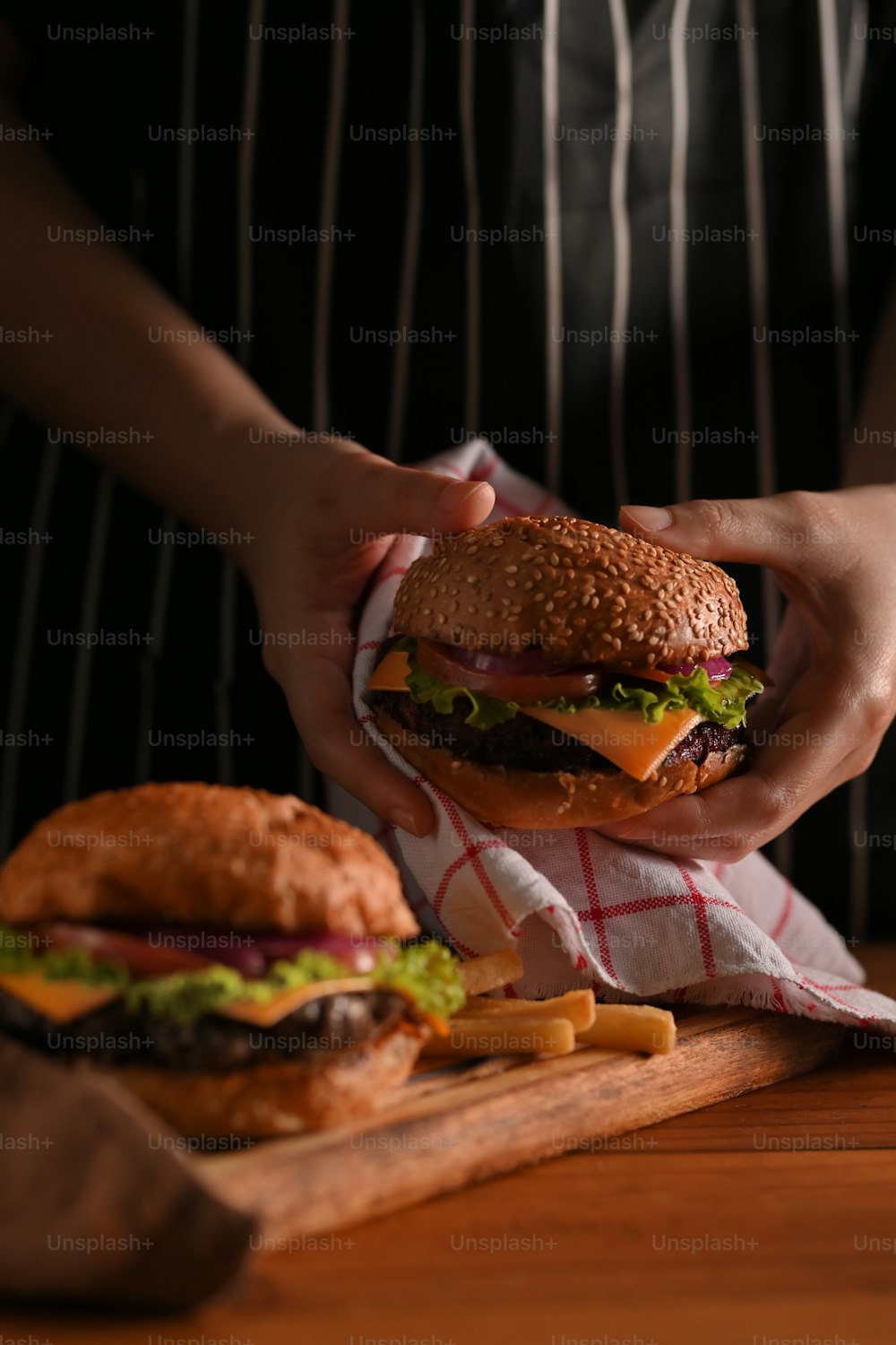 Close-up view of woman holding beef burgers with napkin in restaurant with black wall background
