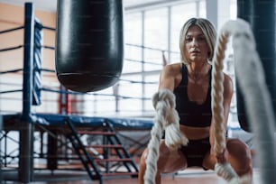 On the way to perfect body and health. Blonde sport woman have exercise with ropes in the gym. Strong female.