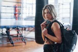 Serious look. Adult female with black bag and headphones in the training gym.