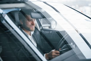 Persona amable y positiva. Hombre de negocios moderno probando su nuevo automóvil en el salón del automóvil.