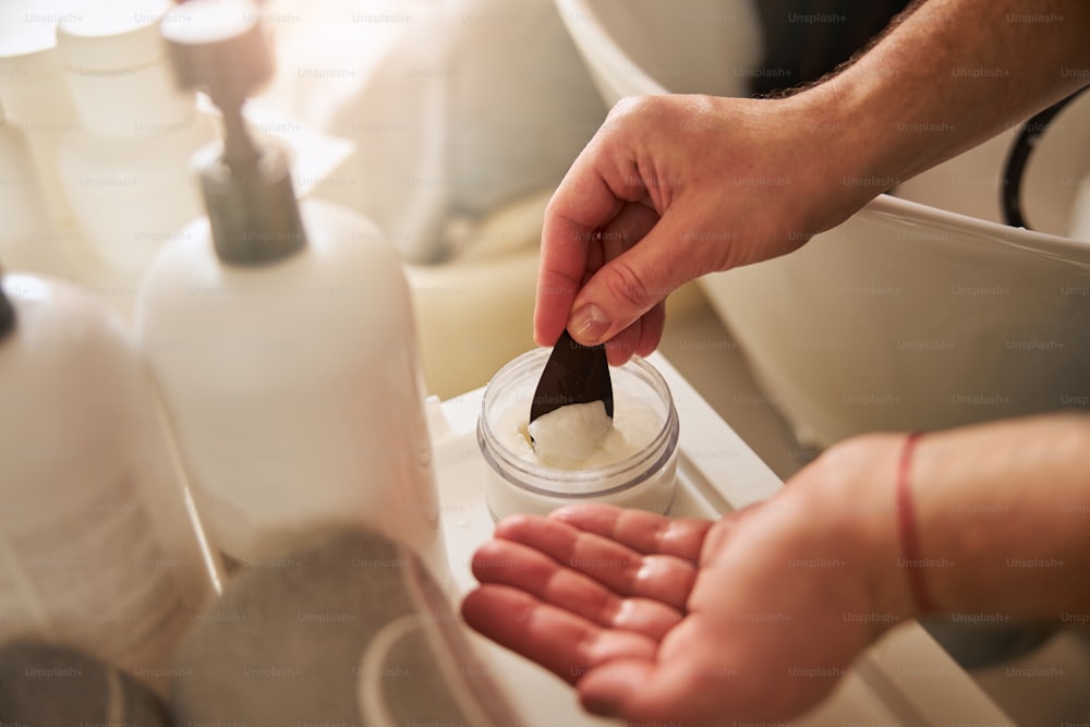 Cropped photo of a professional hairdresser scooping out a dollop of hair mousse from the glass jar