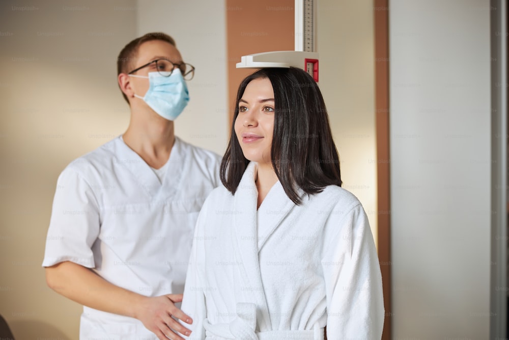 Smiling pleased lovely young Caucasian woman in a terry bathrobe leaning against the height rod