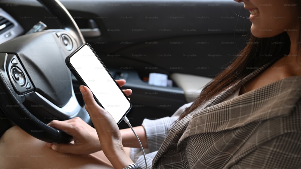 차를 운전하는 동안 lank 스크린으로 스마트폰을 들고 있는 젊은 여성의 잘린 샷.