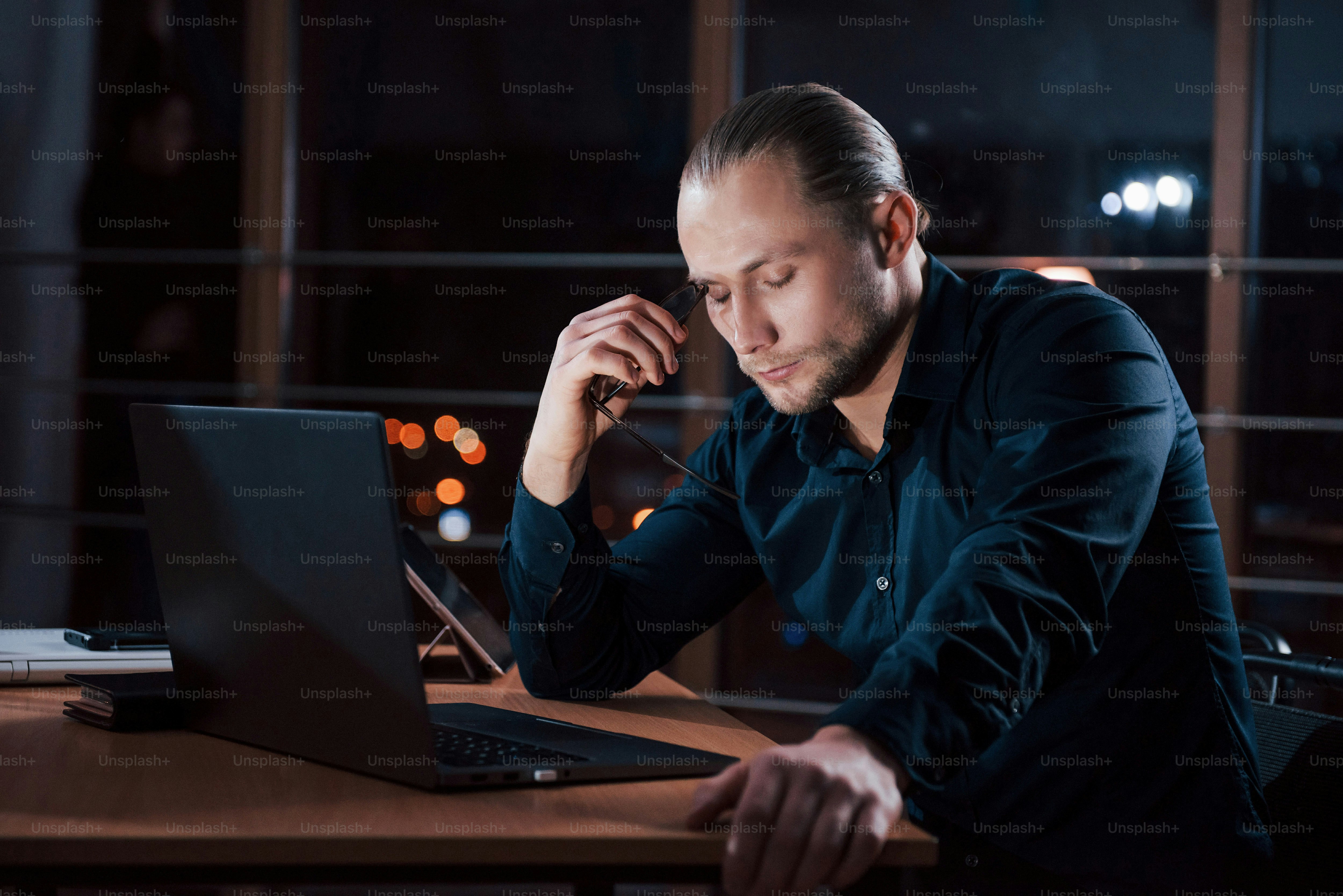 Can't work more, need to rest. Stylish businessman in eyewear sits alone in the office at nightime.