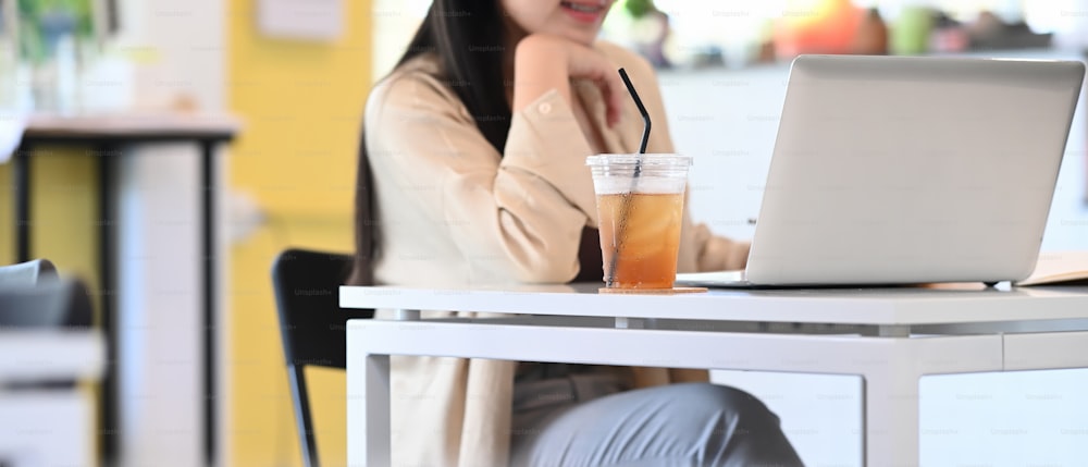 Cropped shot of young female entrepreneur thinking about her project and working with computer laptop while sitting in coffee shop.