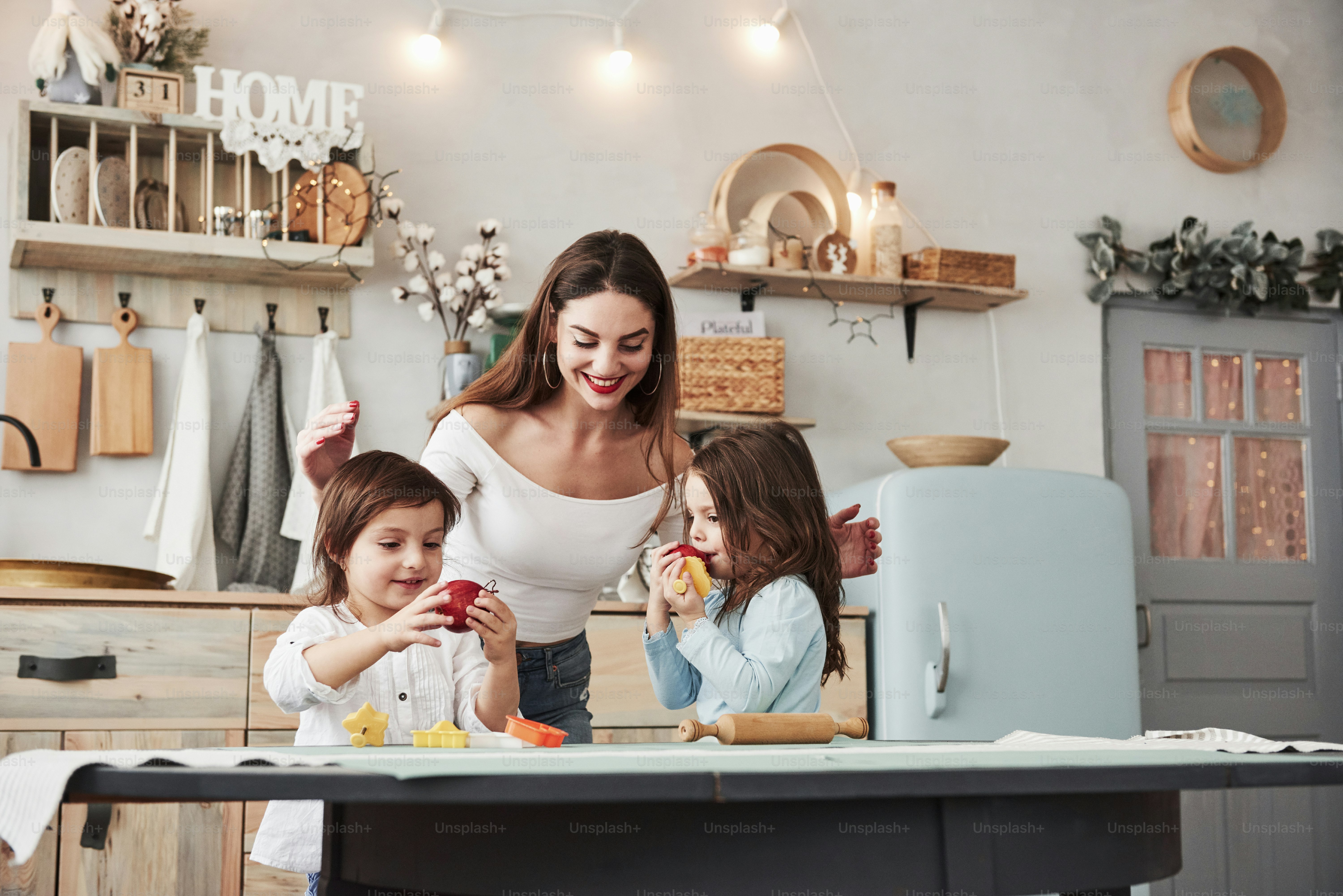 Manger des fruits frais. Une belle jeune femme nourrit deux enfants avec des pommes pendant qu’ils sont assis près de la table avec des jouets.