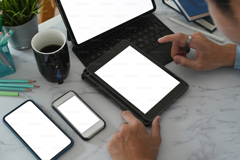 Close up view of young man using multiple devices with empty screen on marble table. Blank screen for your advertising text.