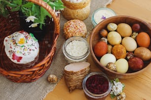 Traditional Easter food for blessing, homemade Easter bread, stylish easter eggs and blooming spring flowers on linen napkin on rustic table. Happy Easter! Festive breakfast