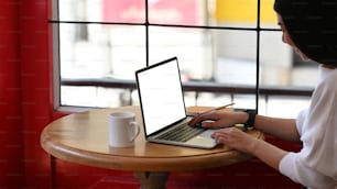 Ausschnittaufnahme einer lächelnden jungen Unternehmerin, die mit einem Computer-Laptop im Café an ihrem Projekt arbeitet.