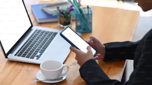 Cropped shot of young businesswoman using smart phone while sitting in front of computer laptop at office.