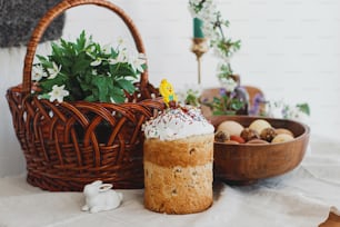 自家製のイースターパン、モダンな天然染めの卵、籐のバスケット、ウサギ、素朴なテーブルに咲く春の花。イースターおめでとう。教会の祝福とお祝いのディナーのための伝統的なイースター料理