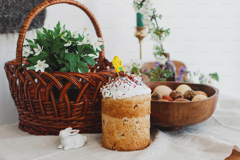 Homemade Easter bread, modern natural dyed eggs, wicker basket, bunny and blooming spring flowers on rustic table. Happy Easter. Traditional easter food for church blessing and festive dinner