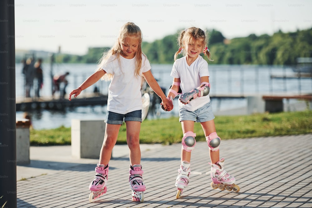 Two cute kids riding by roller skates in the park at daytime.