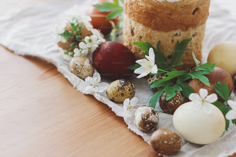 Delicious homemade Easter bread, stylish easter eggs, blooming spring flowers on linen napkin on rustic table. Happy Easter! Space for text. Modern natural dyed eggs and traditional Easter food