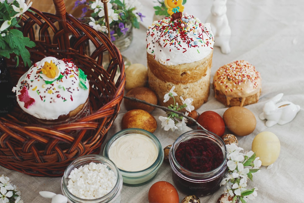 Traditional Easter food for blessing, homemade Easter bread, stylish easter eggs and blooming spring flowers on linen napkin on rustic table. Happy Easter! Festive breakfast