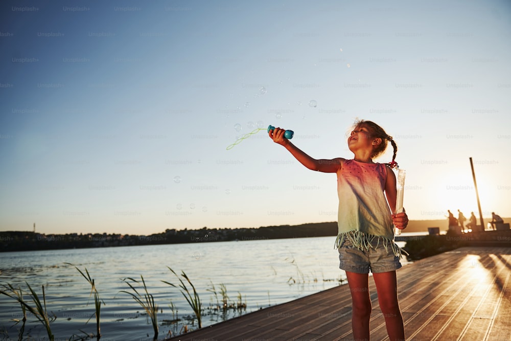 Sera. Bambina felice che gioca con le bolle vicino al lago al parco.