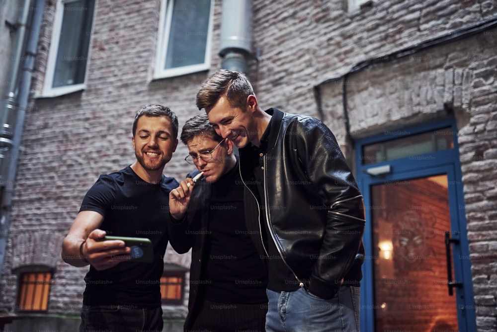 Trois amis masculins se tiennent à l’extérieur du bar. Avoir une conversation. Dans de beaux vêtements.