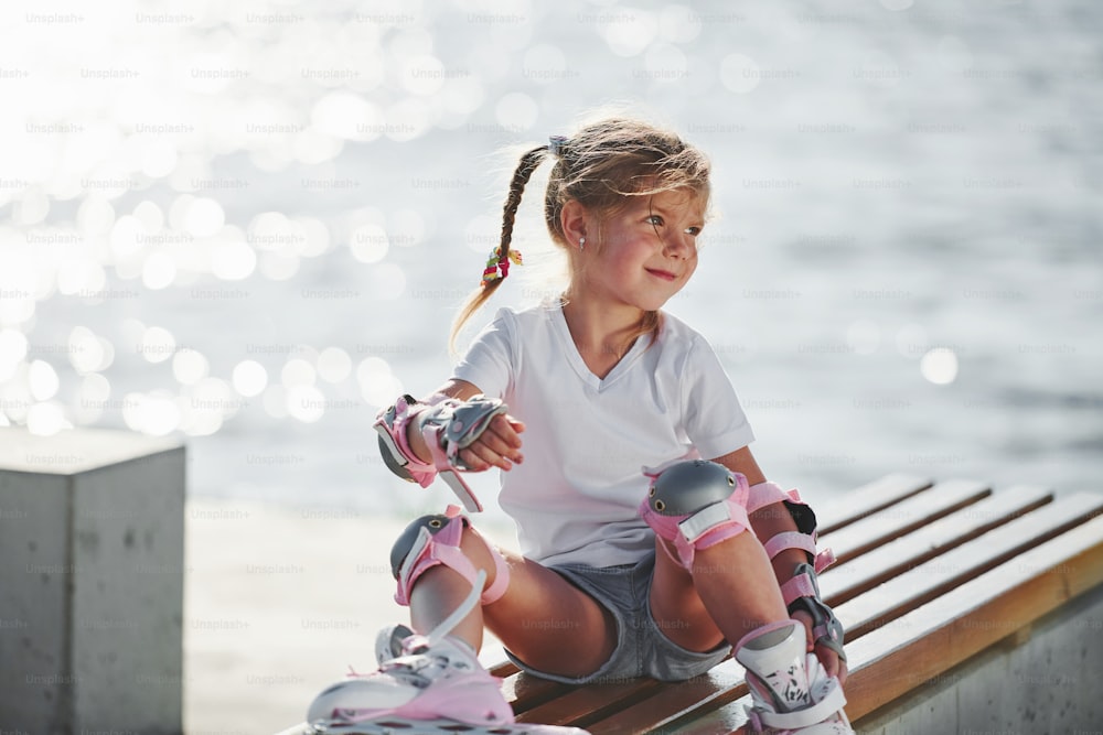 Bambina carina con pattini a rotelle all'aperto vicino al lago sullo sfondo.